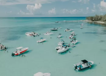 Boats floating on crystal-clear turquoise water near a white sandy coast in the Cayman Islands.