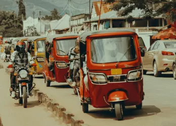 A lively street with red tuk-tuks, people walking, and shops along the roadside.