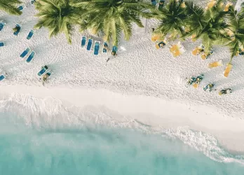A white sandy beach with turquoise water and lush green trees along the shoreline.
