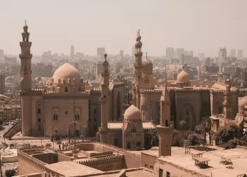 A historic cityscape with mosques, minarets, and sandy-colored buildings.