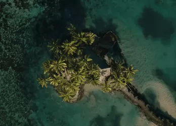 Aerial view of a small tropical island with green forest and coral reefs.