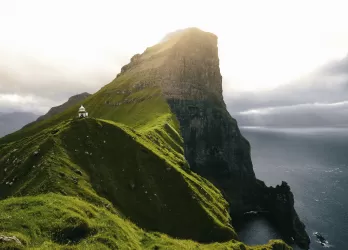 Steep green cliffs rising from the ocean with fog in the background.