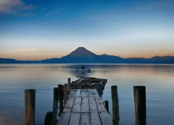 A wooden pier extending into calm waters with a mountain in the distance.