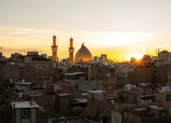 A sunset over Baghdad, Iraq, with mosque minarets silhouetted against the sky.