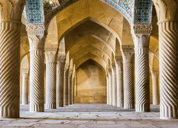 The interior of a historic Persian mosque in Iran with intricate arches and tiles.