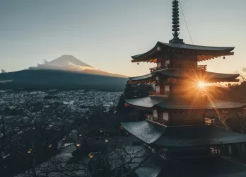 A traditional Japanese pagoda with Mount Fuji in the background during sunset.