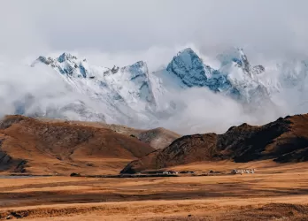 Snow-capped mountains rise over a dry, golden plain in Kyrgyzstan.