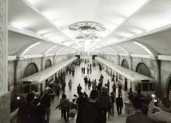 A large metro station hall with chandeliers and people walking.