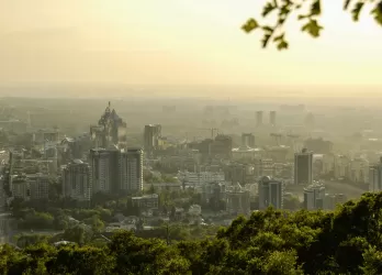 A hazy cityscape of Almaty, Kazakhstan, with buildings surrounded by greenery.