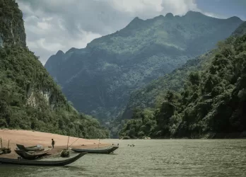 A tranquil river in a lush green valley surrounded by forested mountains, with a traditional boat on the water.