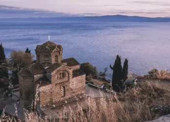 Ancient stone ruins and a church on a hillside with mountains behind.