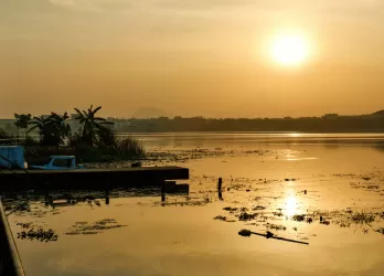 A golden sunset over a wide river with scattered boats and trees.