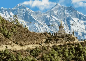 A snow-capped mountains towering above green hills in the foreground.