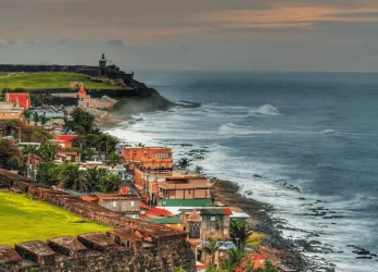 Colorful houses on a hillside by the ocean with waves crashing on the shore.