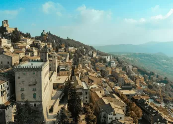 A hillside town with stone buildings and mountains in the distance.