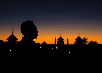 Silhouettes of trees and a person against a deep orange sunset sky.