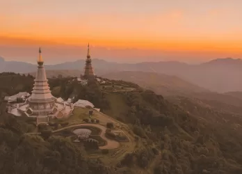 Twin golden pagodas on a hilltop surrounded by forests at sunset.