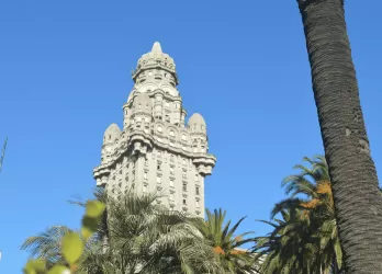 Historic building with intricate tower and palm trees against a blue sky.